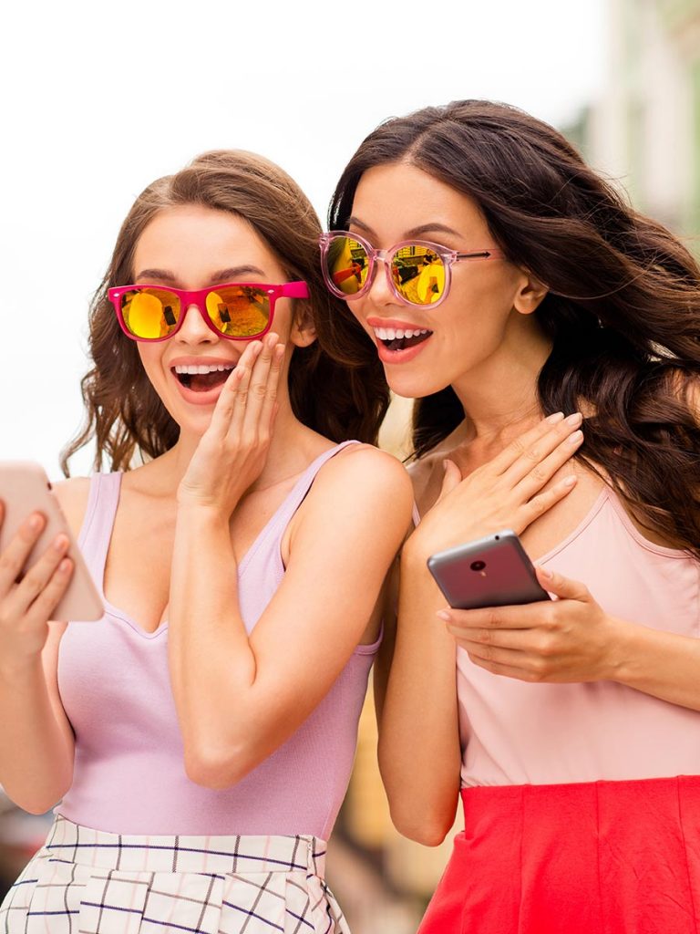 Zwei hübsche Frauen chaten auf ihrem Smartphone